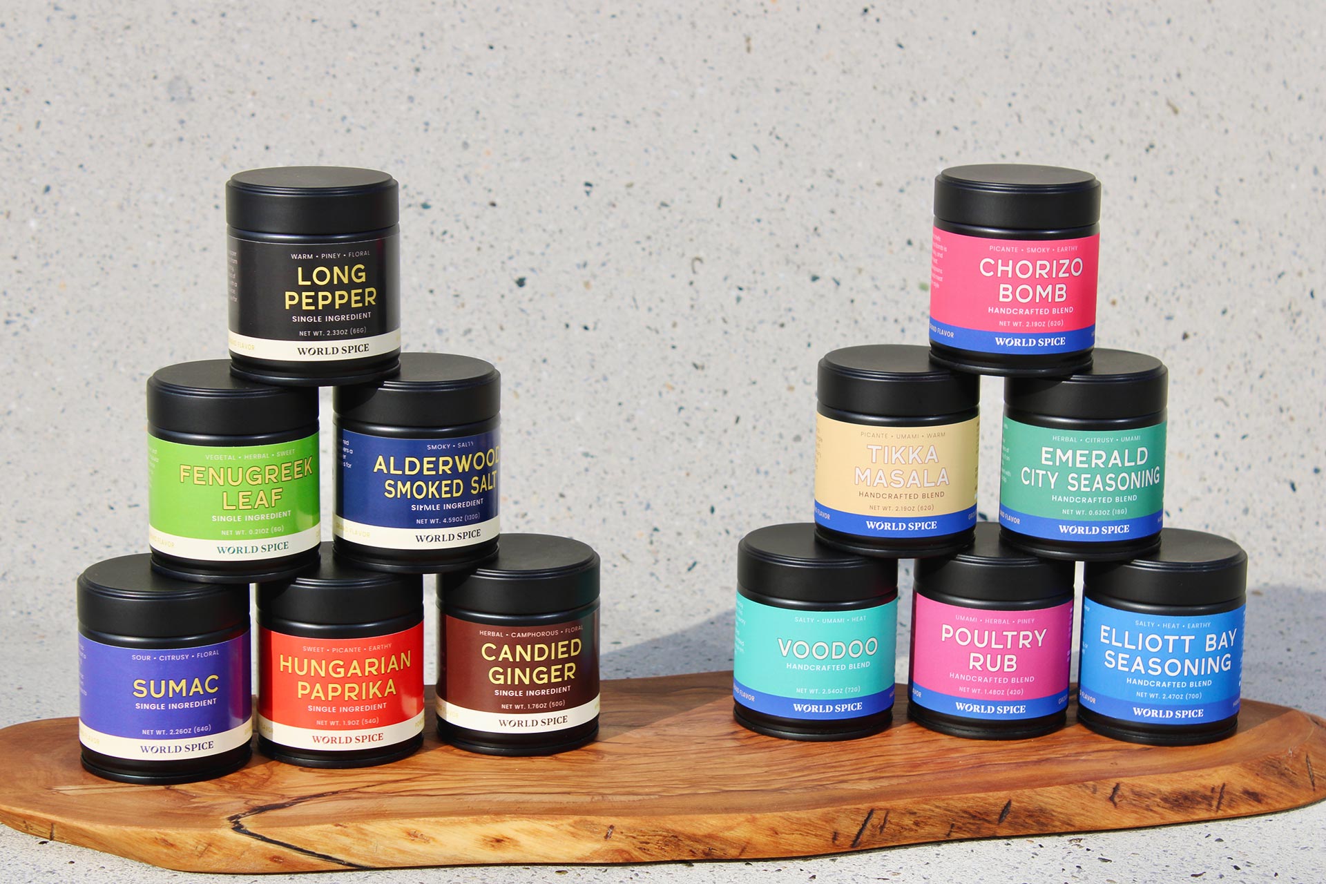 A collection of various spice jars and containers, each with different labels and colors, arranged on a wooden board.